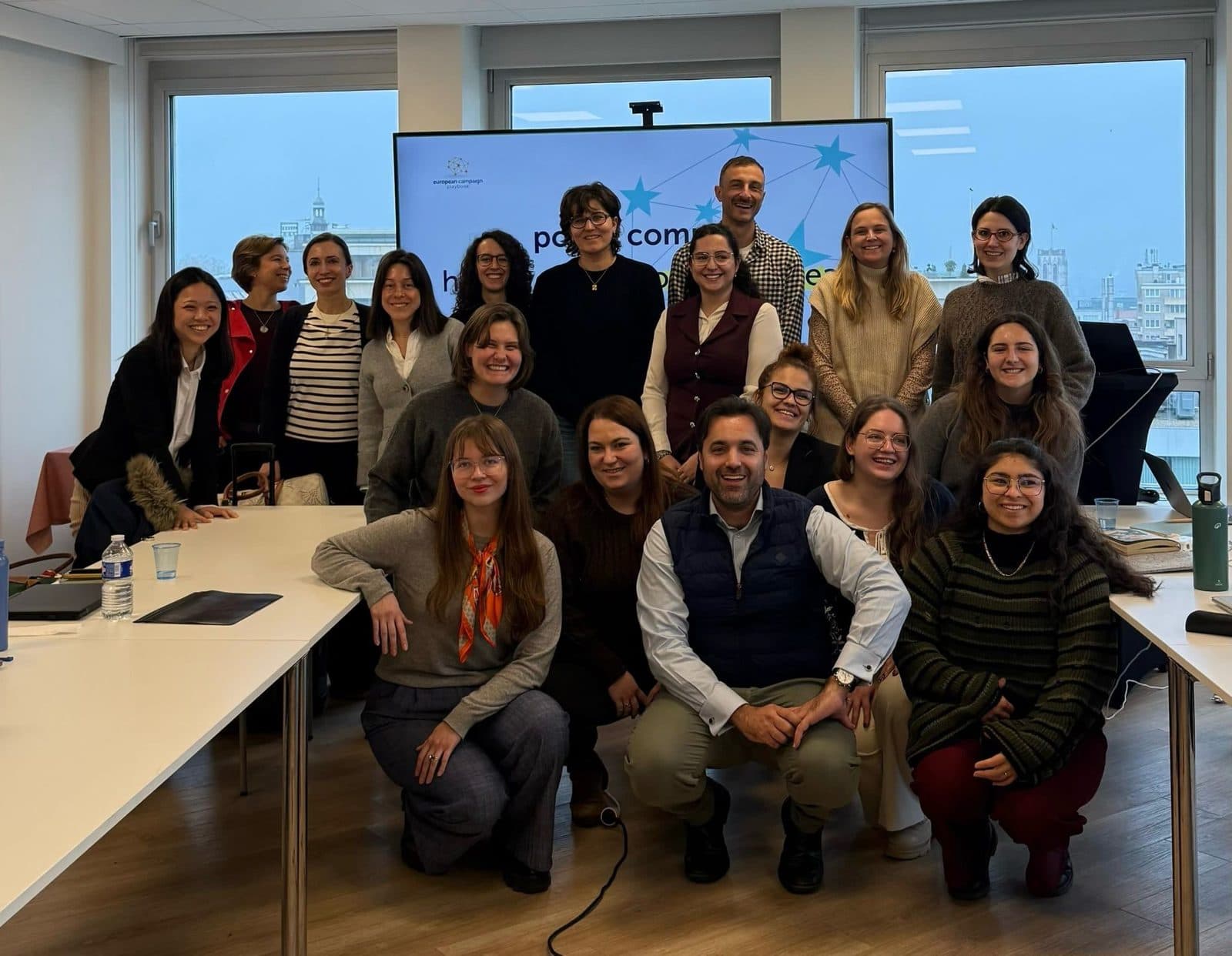 Participants and the trainer pose in front of a screen showing the european campaign playbook logo after a policy communications workshop